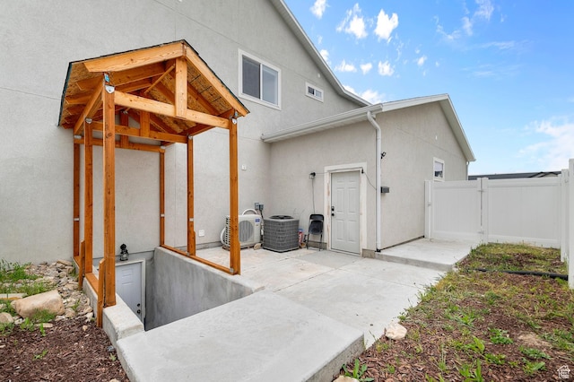 view of side of property with a gate, stucco siding, a patio, fence, and cooling unit