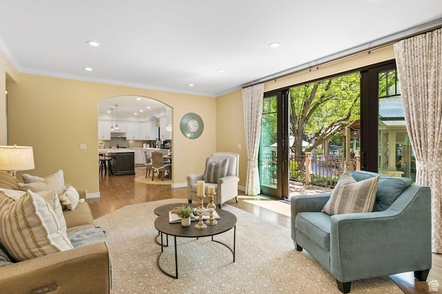 living room featuring arched walkways, light wood finished floors, recessed lighting, ornamental molding, and baseboards