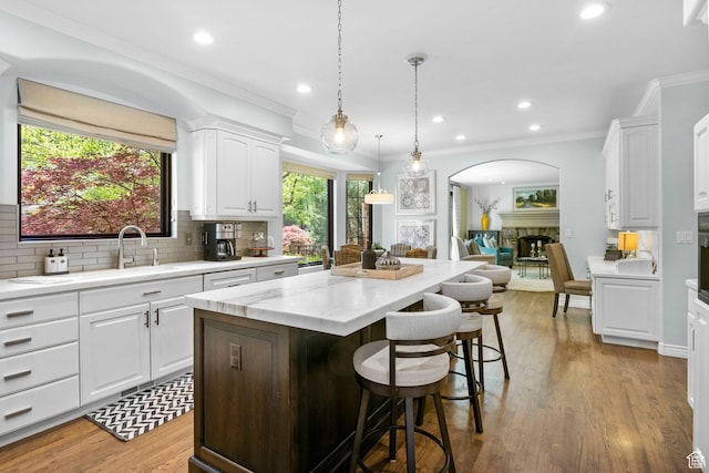 kitchen featuring arched walkways, a stone fireplace, decorative backsplash, a kitchen island, and white cabinetry