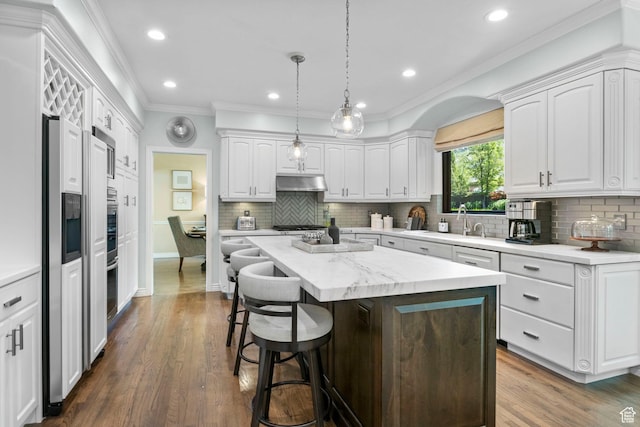 kitchen with ornamental molding, white cabinetry, a kitchen bar, a center island, and a sink
