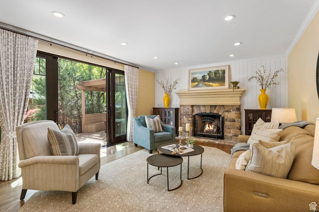 living area featuring ornamental molding, wood finished floors, a stone fireplace, and recessed lighting