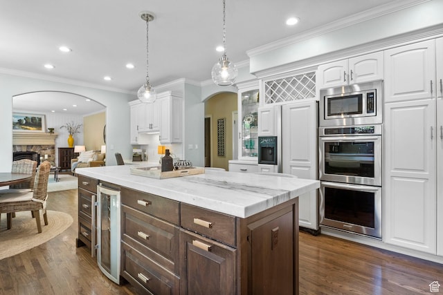 kitchen featuring wine cooler, white cabinetry, arched walkways, a center island, and crown molding