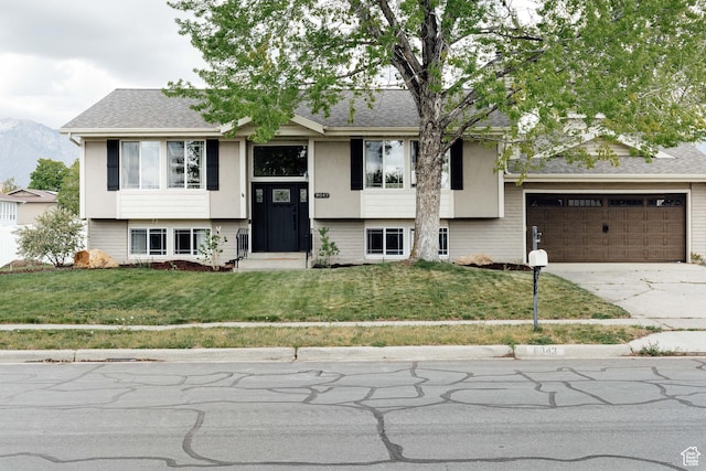 raised ranch featuring driveway, a front lawn, a mountain view, roof with shingles, and a garage
