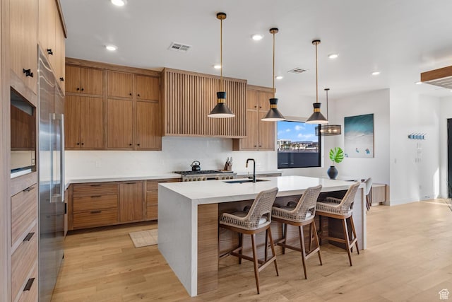 833 W Savoy Ln, St George, UT 84790 - kitchen with a sink, brown cabinetry, light wood-style floors, an island with sink, and recessed lighting