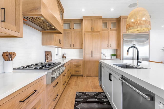 kitchen featuring appliances with stainless steel finishes, custom range hood, light countertops, a sink, and recessed lighting