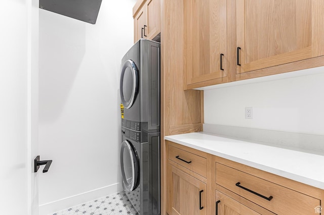 laundry room featuring stacked washing machine and dryer, cabinet space, baseboards, and light flooring