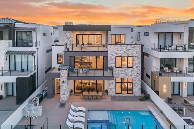 back of property at dusk with stone siding, stucco siding, and an outdoor pool