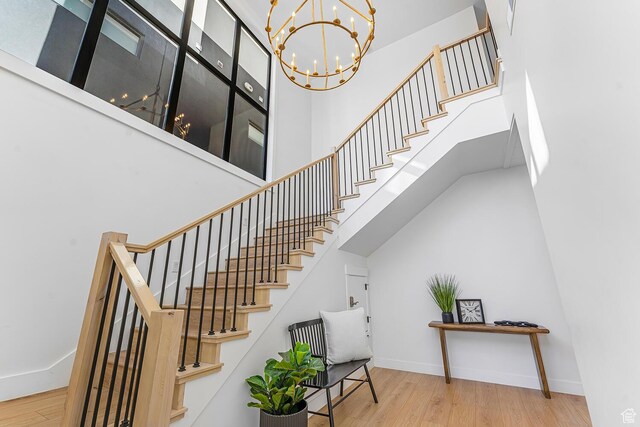 staircase featuring wood finished floors, a chandelier, baseboards, and a high ceiling