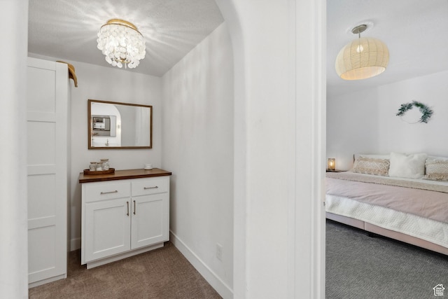 corridor featuring dark carpet, a chandelier, and baseboards