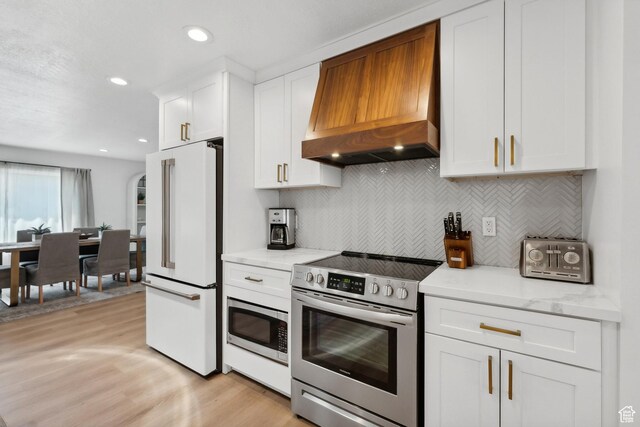 kitchen featuring stainless steel appliances, custom range hood, white cabinetry, light wood-style floors, and decorative backsplash