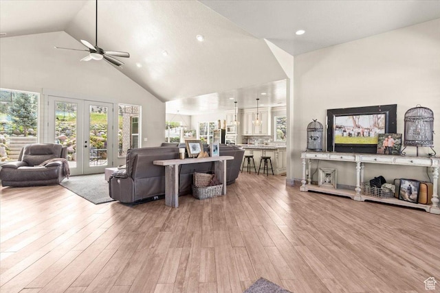 living room with a ceiling fan, high vaulted ceiling, plenty of natural light, light wood finished floors, and french doors