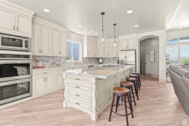 kitchen with stainless steel appliances, healthy amount of natural light, arched walkways, a kitchen bar, and recessed lighting