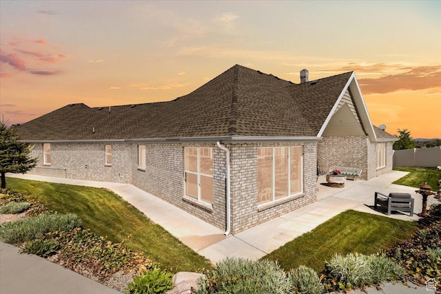 property exterior at dusk with a patio, brick siding, and a shingled roof