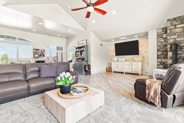 living area with ceiling fan, wood finished floors, recessed lighting, high vaulted ceiling, and a wood stove