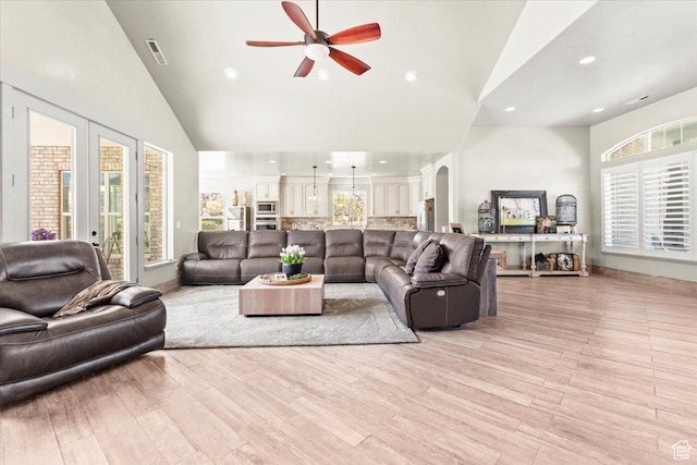 living area featuring high vaulted ceiling, ceiling fan, arched walkways, healthy amount of natural light, and light wood-style floors