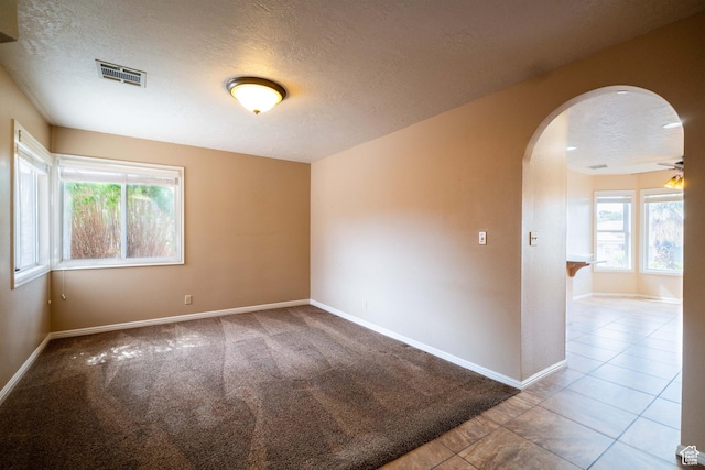 spare room with a textured ceiling, arched walkways, baseboards, tile patterned flooring, and carpet flooring