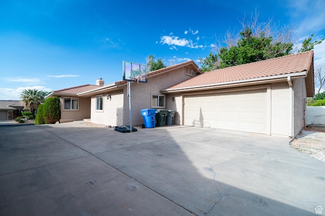 back of house with stucco siding, a tiled roof, an attached garage, and driveway