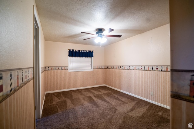 empty room featuring ceiling fan, carpet floors, a wainscoted wall, and a textured ceiling