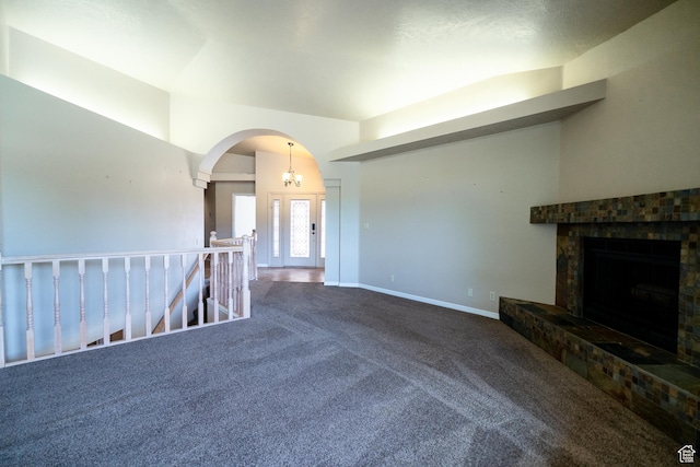 unfurnished living room with carpet floors, a tiled fireplace, arched walkways, and baseboards