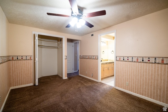 unfurnished bedroom with light carpet, a textured ceiling, a wainscoted wall, a closet, and ceiling fan