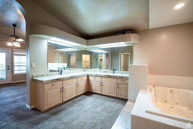 bathroom with lofted ceiling, a jetted tub, double vanity, a ceiling fan, and baseboards
