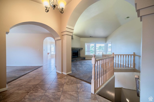 hallway featuring arched walkways, carpet, baseboards, a chandelier, and vaulted ceiling