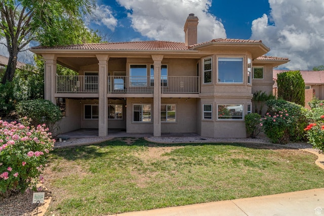 rear view of property featuring a balcony, stucco siding, a tiled roof, a chimney, and a lawn