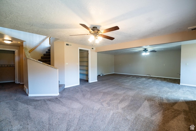 unfurnished living room with ceiling fan, carpet floors, stairs, baseboards, and a textured ceiling