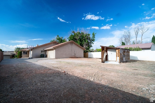 view of front facade with dirt driveway, fence, an attached garage, and a storage unit