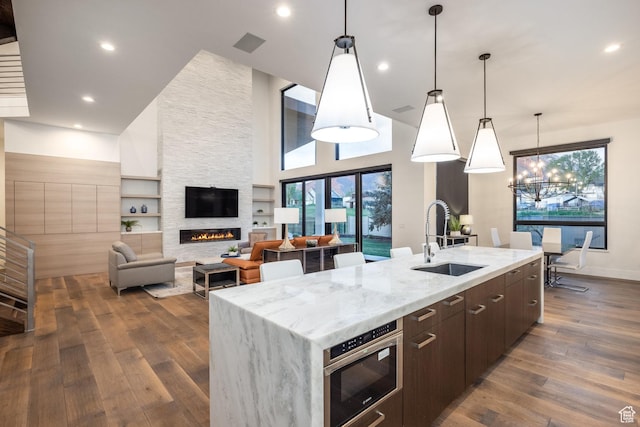 9969 S Altamont Dr E, Sandy, UT 84092 - kitchen featuring a sink, a large island with sink, dark wood-type flooring, dark brown cabinets, and a stone fireplace