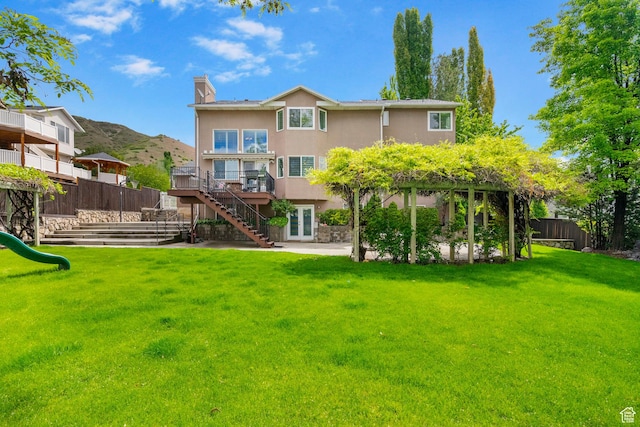 back of property with a playground, stairway, a wooden deck, stucco siding, and a chimney