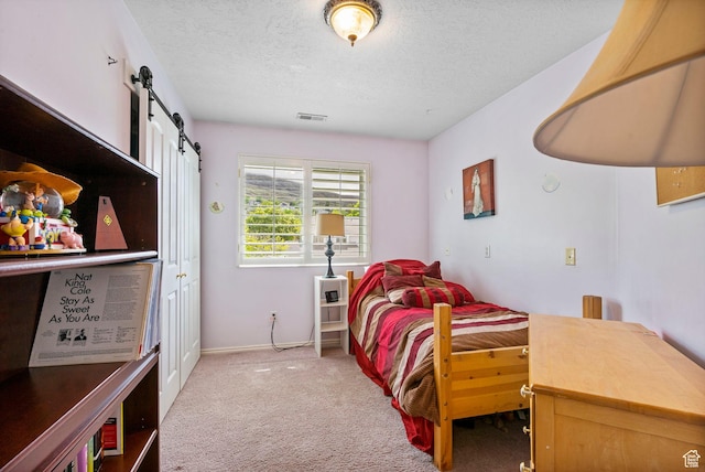 bedroom featuring carpet, a textured ceiling, a barn door, and baseboards