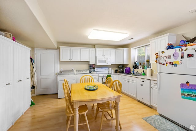 kitchen with white appliances, washing machine and clothes dryer, light wood-style floors, white cabinetry, and light countertops