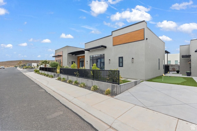 contemporary house with an area to practice putting, fence, and stucco siding