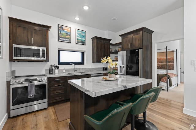 kitchen with appliances with stainless steel finishes, dark brown cabinetry, a sink, light wood-style flooring, and recessed lighting