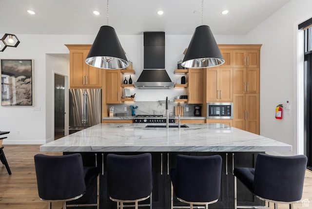 kitchen with wall chimney range hood, freestanding refrigerator, built in microwave, light wood finished floors, and a spacious island
