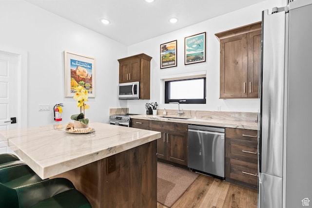 kitchen featuring appliances with stainless steel finishes, a sink, light stone counters, a breakfast bar, and dark brown cabinets