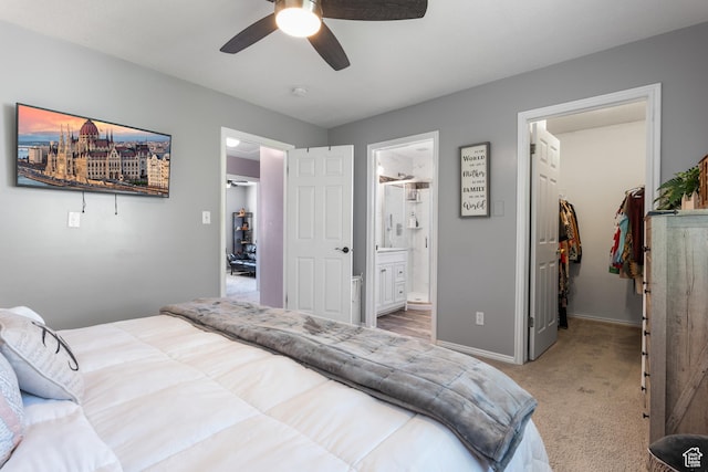 bedroom featuring a walk in closet, a closet, light carpet, ensuite bath, and baseboards