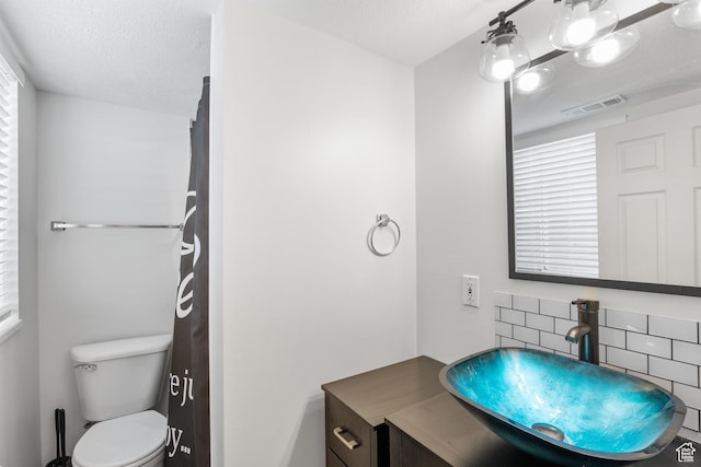 bathroom featuring backsplash, toilet, vanity, and a textured ceiling