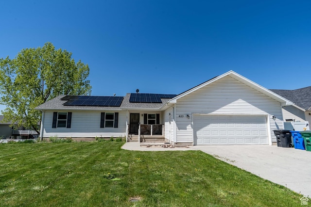 ranch-style house with an attached garage, roof mounted solar panels, a front lawn, concrete driveway, and a shingled roof