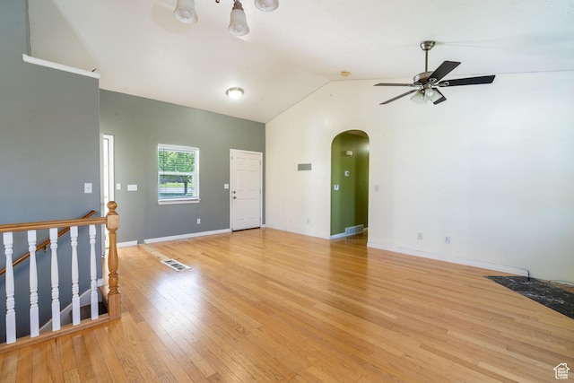 unfurnished living room with arched walkways, ceiling fan, vaulted ceiling, light wood-type flooring, and baseboards