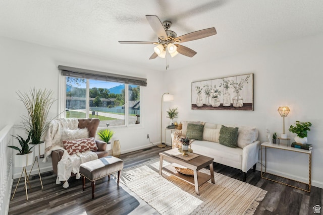 living area with a ceiling fan, dark wood-style floors, baseboards, a textured ceiling, and a water view