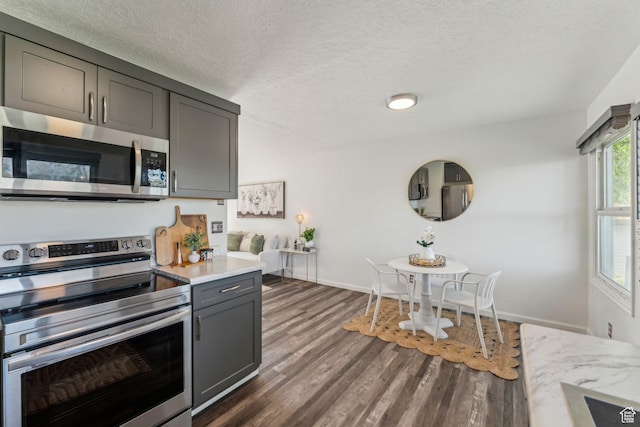 kitchen featuring appliances with stainless steel finishes, light countertops, gray cabinetry, dark wood-style floors, and baseboards