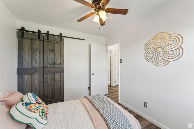 bedroom with wood finished floors, a barn door, baseboards, and ceiling fan