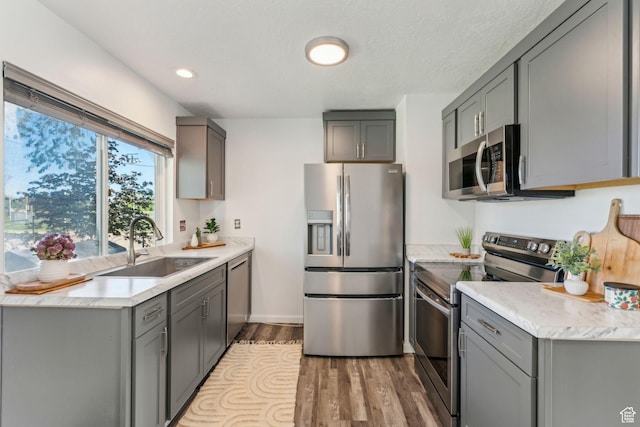 kitchen with appliances with stainless steel finishes, a sink, gray cabinetry, light wood finished floors, and recessed lighting