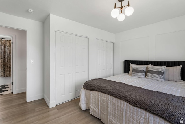 bedroom featuring multiple closets, wood finished floors, baseboards, and a chandelier