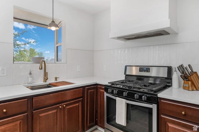 kitchen featuring stainless steel gas stove, a sink, custom exhaust hood, decorative backsplash, and light countertops
