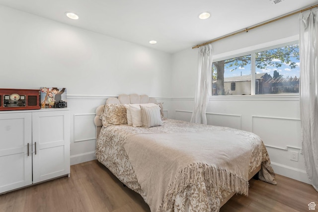 bedroom featuring wood finished floors, recessed lighting, baseboards, and a decorative wall