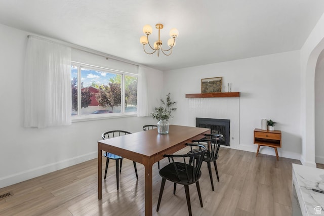 dining space featuring a fireplace, a chandelier, light wood finished floors, and baseboards