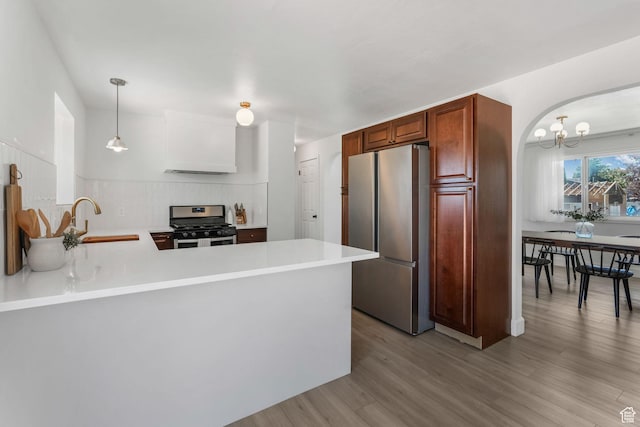 kitchen featuring stainless steel appliances, light wood-style floors, a sink, light countertops, and a peninsula